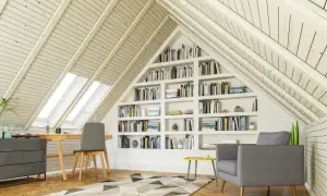 Gemütlicher Arbeitsplatz mit Bücherregalen im Dachausbau. Ein Schreibtisch unter Dachfenstern und eine Leseecke laden zum Verweilen ein.