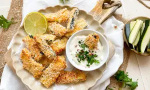 Knusprige Zucchini Pommes, paniert und goldbraun gebacken, serviert mit Dip und Limette.
