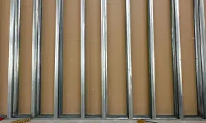 Metalowe profile UW tworzą szkielet ścianki działowej. W tle brązowe płyty.