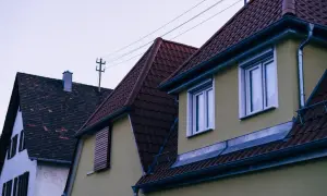 Toits en tuiles de couleur bordeaux, avec une charpente fermette visible sous les toits. Des fils électriques traversent le ciel.