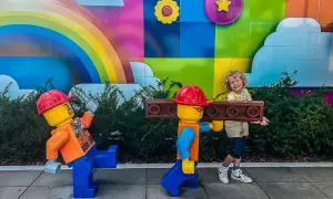 Chłopiec z uśmiechem pozuje z dwoma wielkimi ludzikami LEGO na tle kolorowego muralu. To świetne billund atrakcje dla całej rodziny!