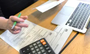 Osoba wypełnia dokumenty ZUS, obok leży kalkulator i laptop. Prawdopodobnie chodzi o zasiłek opiekuńczy.