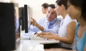 Uomo indica schermo a collega, mentre lei digita. Un tirocinio extracurriculare con stipendio è un'ottima opportunità.