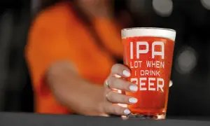 Un bicchiere di IPA con la scritta "IPA LOT WHEN I DRINK BEER" tenuto da una mano con unghie bianche.