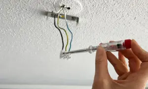 Hand mit Schraubendreher prüft Kabel für die Montage einer Lampe an der Decke.