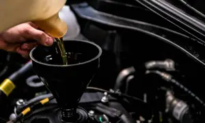 Main d'un mécanicien versant de l'huile neuve dans un moteur pour éviter une fuite d'huile moteur.