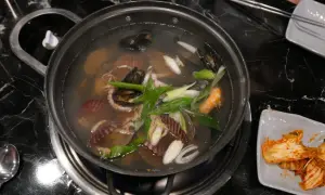Un plat de cuisson de fruits de mer mijote dans un bouillon, avec des moules, des crevettes, des pétoncles et des poulpes.