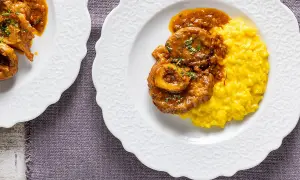 Ossobuco ricetta originale servito su un piatto bianco con risotto giallo allo zafferano.