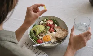 Persona prende una capsula di vitamina D, chiedendosi se sia meglio vitamina d quando prenderla mattina o sera, accanto a un piatto salutare.