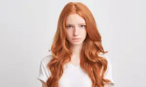 Dziewczyna z burzą włosów w odcieniu rudy, z piegami na nosie, patrzy prosto przed siebie.