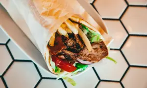 Duży kebab w tortilli z mięsem, frytkami, sałatą i pomidorem na białym talerzu.