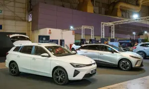Białe kombi MG5 z otwartą klapą bagażnika i srebrny SUV MG na wystawie samochodowej.