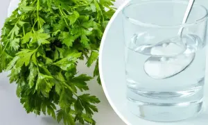 Pietruszka zielona, świeża i aromatyczna, obok szklanki wody z łyżeczką.