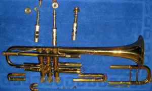 Rozłożona trąbka, instrument dęty blaszany, leży na niebieskim tle. Widać jej poszczególne części: korpus, wentyle, ustnik i inne elementy.