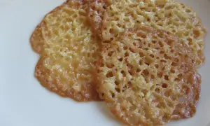 Tre gyllene havreflarn utan sirap ligger på en vit tallrik. De är tunna och krispiga med ett vackert nätmönster.