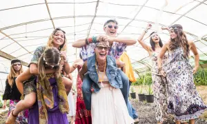 Grupa przyjaciół w stylu hippie świętuje w szklarni, śmiejąc się i bawiąc.