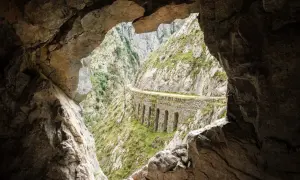 Vista desde una cueva de la ruta del Cares, con un camino tallado en la roca y arcos de piedra.