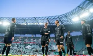 Piłkarze w czarnych strojach stoją na boisku. Jeden z nich ma opaskę w barwach narodowych. Czy to oznacza, że przegrali mecz i dostali walkower? Co to znaczy?