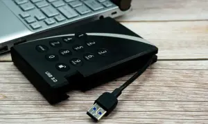 Dysk zewnętrzny z klawiaturą numeryczną i kablem USB 3.0 obok laptopa, gotowy do udostępniania internetu z telefonu na komputer przez USB.