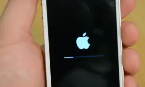 Dłoń trzyma iPhone'a z logo Apple i paskiem postępu, wskazującym na proces hard reset iPhone.