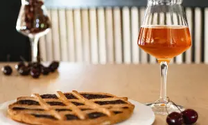 Torta con marmellata di ciliegie e un bicchiere di birra alla ciliegia, con ciliegie fresche sparse sul tavolo.