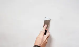 Mano con spatola applica stucco bianco su parete, un passo per come pitturare di bianco una parete gialla.