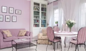 Jasny salon z fioletową kanapą i krzesłami w różowe pasy. Kolor lawendowy ścian świetnie komponuje się z bielą mebli i zasłon, tworząc przytulną atmosferę.