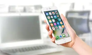 Dłoń trzyma iPhone'a z ikonami aplikacji. Dowiedz się, jak włączyć lokalizację w przeglądarce iPhone, aby korzystać z map i innych funkcji.