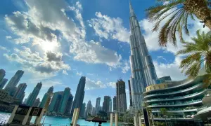 Burdż Chalifa góruje nad Dubajem. Zdjęcia ukazują drapacze chmur, błękitne niebo z chmurami i palmy.