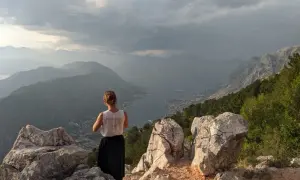 Kobieta podziwia zapierające dech w piersiach czarnogóra widoki z góry. W dole zatoka i miasteczko.