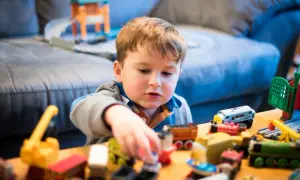 Bambino concentrato nel suo gioco del far finta con tanti trenini e costruzioni colorate.
