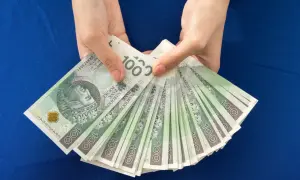Ręce trzymają stos banknotów 100 zł. Zastanawiasz się, ile dać na 50 urodziny? Taka kwota to dobry początek!