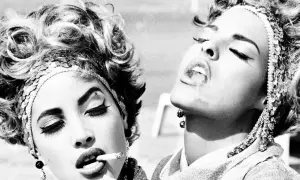 Iconica **Helmut Newton moda**: due donne con acconciature voluminose e make-up audace fumano sigarette, un'immagine di stile e provocazione.
