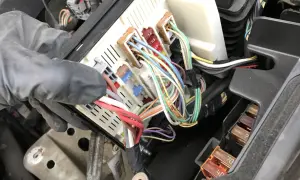 Ręka w rękawiczce manipuluje skrzynką z bezpiecznikami w Renault Scenic 2. Widać kolorowe przewody i oznaczenia bezpieczników.