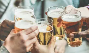 Brindisi con birra, un piacere che, si dice, la birra fa ingrassare. Mani che sollevano bicchieri dorati con schiuma bianca.