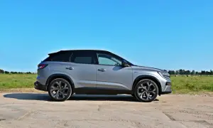 Srebrny Renault Austral z czarnym dachem stoi na drodze polnej, w tle zielone pole i błękitne niebo.