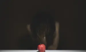 Czerwone jabłko na białym tle, w tle niewyraźna postać pochylona nad nim.