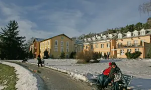 Żółty budynek sanatorium otoczony śniegiem, ludzie siedzą na ławce.