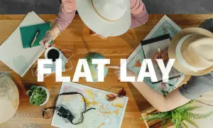 Widok z góry na stół z mapami, globusem, aparatem i notatkami. Dwie osoby planują podróż. To idealny **flat lay** do inspiracji.