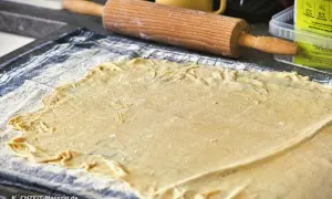 Dünn ausgerollter Strudelteig liegt auf einem Küchentuch, bereit für ein köstliches Strudel-Rezept. Ein Nudelholz liegt daneben.