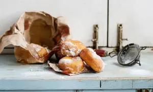 Pączki posypane cukrem pudrem, częściowo w papierowej torbie. Wskazówki, jak przechowywać pączki, by były świeże.