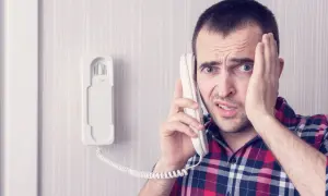 Zmartwiony mężczyzna dzwoni z telefonu domofonowego. Gdzie zgłosić niedziałający domofon?