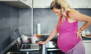 Gravid kvinna med ont i ryggen, hon kan inte gå p.g.a. foglossning. Hon står vid en bänk med en laptop.