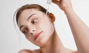Kobieta aplikuje kroplę serum na skroń. To esencja piękna, która odżywia skórę.