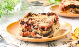 Porción de lasaña de berenjena horneada, con capas de berenjena, salsa de tomate y queso derretido, servida en un plato naranja.