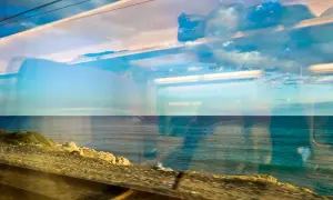 Blick aus dem Zugfenster auf das Meer. Die Spiegelungen im Glas zeigen Wolken und den Himmel, während draußen die Küste vorbeizieht. Mit dem Zug ans Meer ist ein Erlebnis.