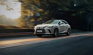 Biały Lexus RX 500h pędzi po drodze, otoczony rozmytymi drzewami i światłem zachodzącego słońca.
