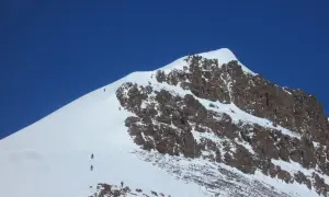 Grupa alpinistów wspina się na najwyższy szczyt Grenlandii, pokonując śnieżne zbocza i skaliste fragmenty.