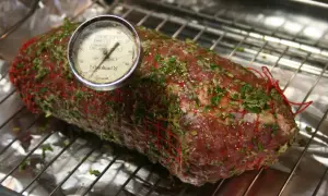 En fransyska i ugn, förberedd för låg temperaturstekning. Köttet är nätat och har en örtmarinad. En köttermometer visar temperaturen.