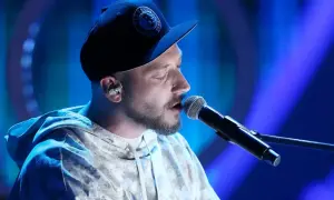 Artysta w czapce z daszkiem śpiewa do mikrofonu. W jego oczach widać emocje, jakby opowiadał historię: "kortezy co w tobie i we mnie".